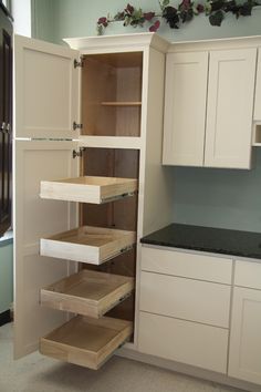 an open cabinet in a kitchen with white cupboards and black counter tops, is shown