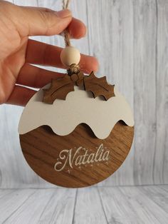 a hand holding a wooden ornament with the name nattella on it