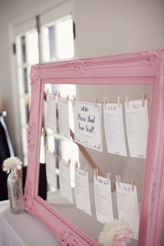 a pink framed mirror with clothes pins attached to it and flowers in a vase on the table