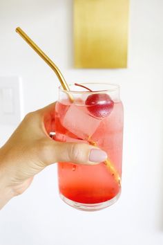 a person holding a glass with a cherry on the rim and a straw in it