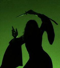 the silhouette of a woman holding a knife in one hand and a pair of scissors in the other