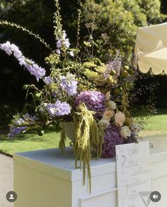 an arrangement of flowers sitting on top of a white box in the middle of a park