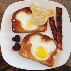 two pieces of toast with an egg and bacon on them, sitting on a plate