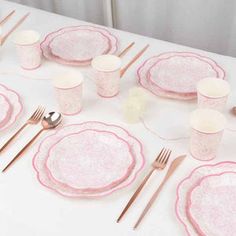 the table is set with pink and white plates, silverware, and napkins