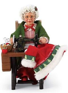 an old woman sitting at a table with a sewing machine and christmas stockings on it