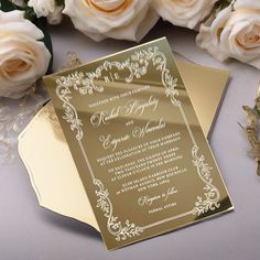 an elegant wedding card with gold foil and white flowers on the table next to it