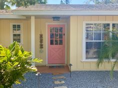 a pink door sits in front of a yellow house with white windows and palm trees