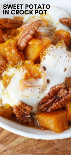 sweet potato in crock pot with pecans and cream on top, sitting on a wooden table