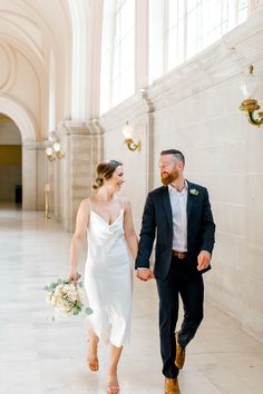 a bride and groom holding hands walking down the hall