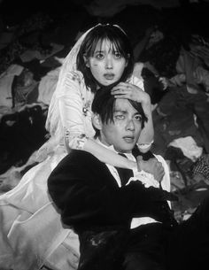 a man sitting next to a woman on top of a bed covered in sheets and blankets