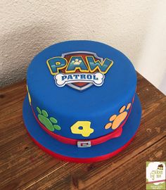 a blue cake with paw patrol on it sitting on top of a wooden table next to a white wall