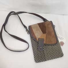 a brown and black handbag sitting on top of a white bed next to a tag