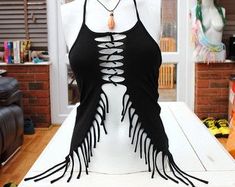 a white mannequin wearing a black top with tassels