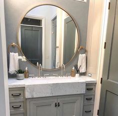 a bathroom with a large round mirror above the sink and marble counter top below it