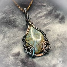 Adorned with a mesmerizing ocean jasper boasting windows of druzy that glisten like sunlight on the water's surface, this pendant exudes an ethereal allure. Its swirly copper design evokes the mysterious charm of the creature from the black lagoon, weaving a tale of enchantment and intrigue. Let this pendant be your talisman of the sea, guiding you through a realm of magic and wonder where the boundaries between reality and fantasy blur, and the secrets of the deep unfold in shimmering splendor. Wire Wrapped Ocean Jasper Pendant Necklaces, Wire Wrapped Ocean Jasper Pendant Jewelry, Wire Wrapped Ocean Jasper Pendant Necklace, Ocean Jasper Wire Wrapped Pendant Necklaces, Healing Ocean Jasper Pendant Jewelry, Artisan Ocean Jasper Jewelry As Gift, Artisan Ocean Jasper Jewelry For Gifts, Ocean Jasper Gemstone Pendant Jewelry, Ocean Jasper Gemstone Pendant