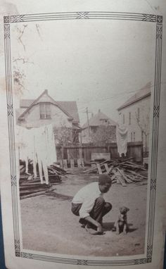 an old black and white photo of a boy playing with a dog