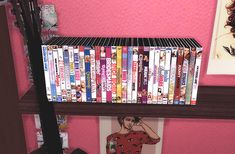 there is a shelf with many movies on it in the corner next to a pink wall