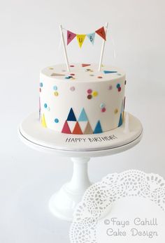 a birthday cake decorated with flags and confetti on a white pedestal next to a doily