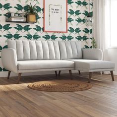 a white couch sitting on top of a hard wood floor next to a wall with green leaves