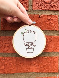 a hand embroidered picture of a person holding a potted plant in front of a brick wall