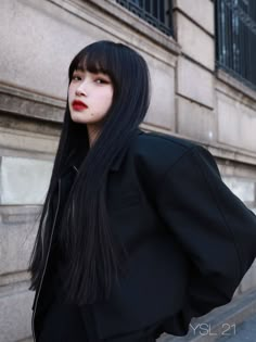 a woman with long black hair and red lipstick standing in front of a stone building