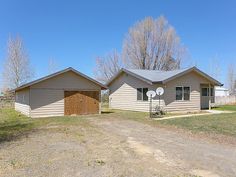 two houses in the middle of a dirt road with trees and grass on both sides