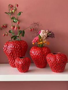 four red vases with flowers in them on a shelf