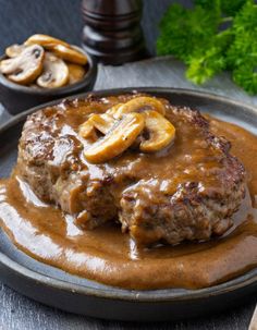 a hamburger covered in gravy and sliced banana's on a plate next to some mushrooms