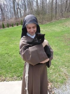 a nun holding a black cat while standing on top of a cement slab in the grass