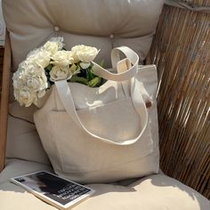 a white tote bag sitting on top of a chair next to a book and flowers