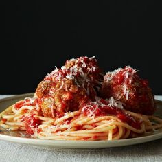 two meatballs covered in sauce and parmesan cheese sit on top of spaghetti