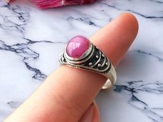 This vintage sterling silver ring features a beautiful cabochon-cut pink Star ruby gemstone, measuring 8mm x 10mm. The ring is made of 925 sterling silver and is tension setting  around a domed ruby design. It is a handmade piece of fine jewelry. The ring is in great vintage condition. The ring size is 8.5, making it suitable for men or women who love antique jewelry with an art theme. Get this unique and one-of-a-kind piece to add to your collection today! Pink Round Cabochon Ruby Ring, Pink Cabochon Ruby Ring, Pink Cabochon Ruby Ring Gift, Tension Setting, Pink Star, Vintage Sterling Silver Rings, Art Theme, Star Ruby, Pink Stars