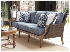 a blue couch with pillows on top of it next to a table and chairs in front of a stone wall