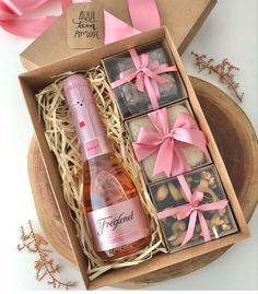 a bottle of wine and some cookies in a box with pink ribbon around the edges