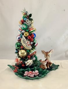 a small christmas tree with ornaments on it and a deer figurine next to it