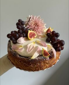 a cake with fruit and flowers on top is being held up by a wooden stick