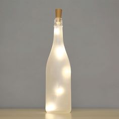 a bottle with some lights in it on a table next to a gray wall and floor