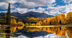 a lake surrounded by trees with mountains in the background and clouds in the sky above