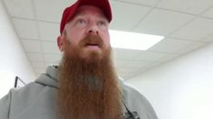 a man with a long beard wearing a red hat and grey sweatshirt in an office