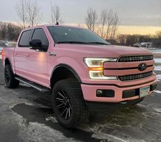 a pink truck is parked in the parking lot with snow on the ground and trees behind it