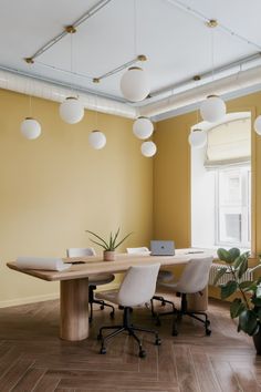 an office with yellow walls and wooden floors, white lamps hanging from the ceiling over a long table