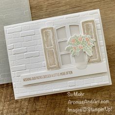 a card with some flowers in it on top of a wooden table next to a window