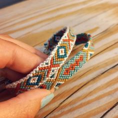 a hand holding two bracelets on top of a wooden table