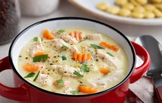 a red bowl filled with chicken and carrots on top of a table next to silverware