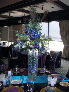 a table set up with plates, silverware and flowers in a tall glass vase