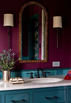 a bathroom with purple walls, blue cabinets and a gold framed mirror above the sink