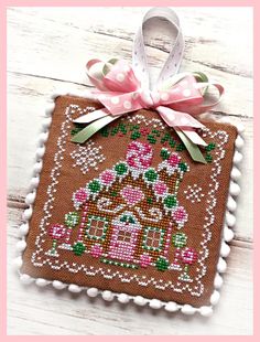 a cross stitch ornament with a house on it and a pink bow hanging from the front