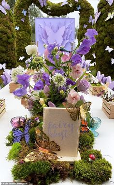 a table topped with lots of purple flowers and butterflies next to a sign that says happy birthday