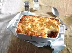 a casserole dish with meat and cheese in it on a table next to two salt shakers