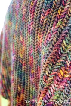 a colorful knitted shawl draped over a wooden table with grass in the background